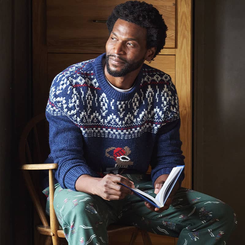 FatFace men's blue Fair Isle knitted Christmas jumper, styled casually with green printed pyjama bottoms.