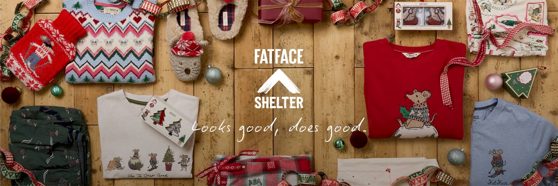 FatFace x Shelter Christmas charity gifts collection flat lay including festive red mouse jumper, fairisle sweater, slippers, and winter pyjamas arranged on wooden boards.