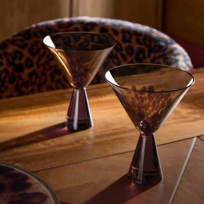 Two tortoiseshell cocktail glasses on a wooden table